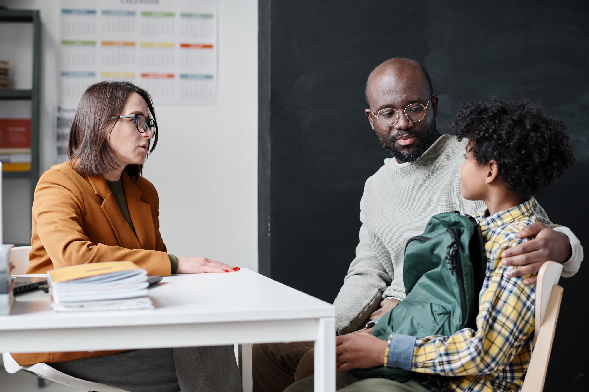 Una maestra y un padre conversando con un niño sobre la coordinación escolar